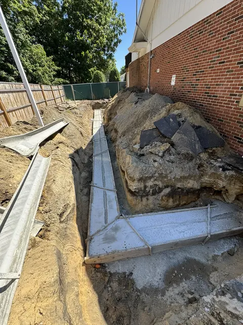 A new concrete footing poured along a brick wall.