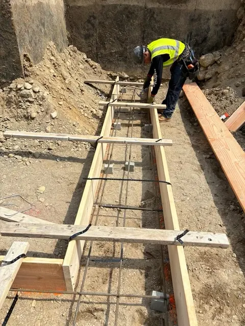 A crew member setting footing forms and rebar for a house addition.